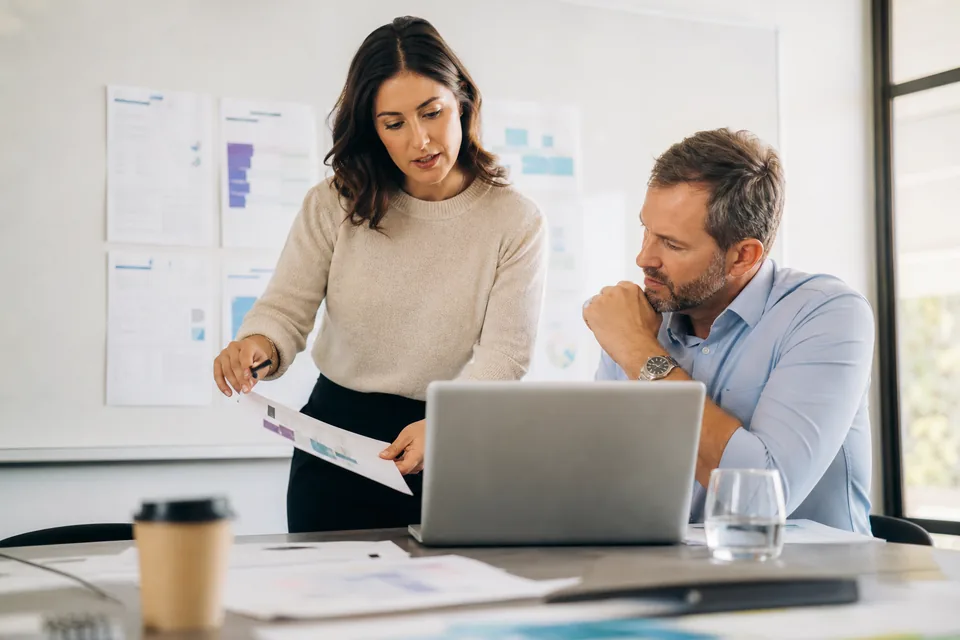 Product marketing manager and sales enablement lead reviewing a competitive battlecard and a software budget