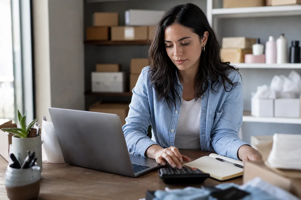Marketer comparing ad research subscription costs with a calculator at a home office desk