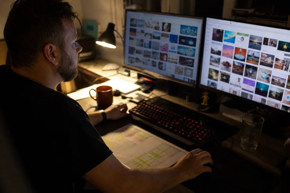 Media buyer reviewing grids of banner and native ad thumbnails on two monitors at a home desk